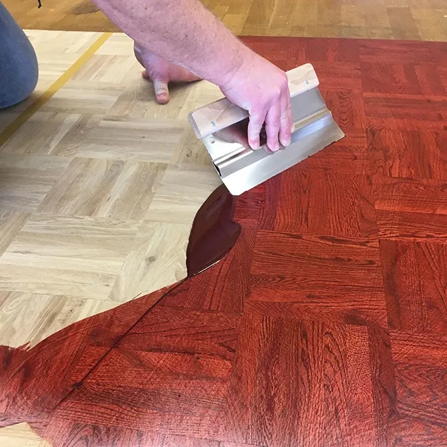 Application d’une huile teintée rouge sur un parquet mosaïque